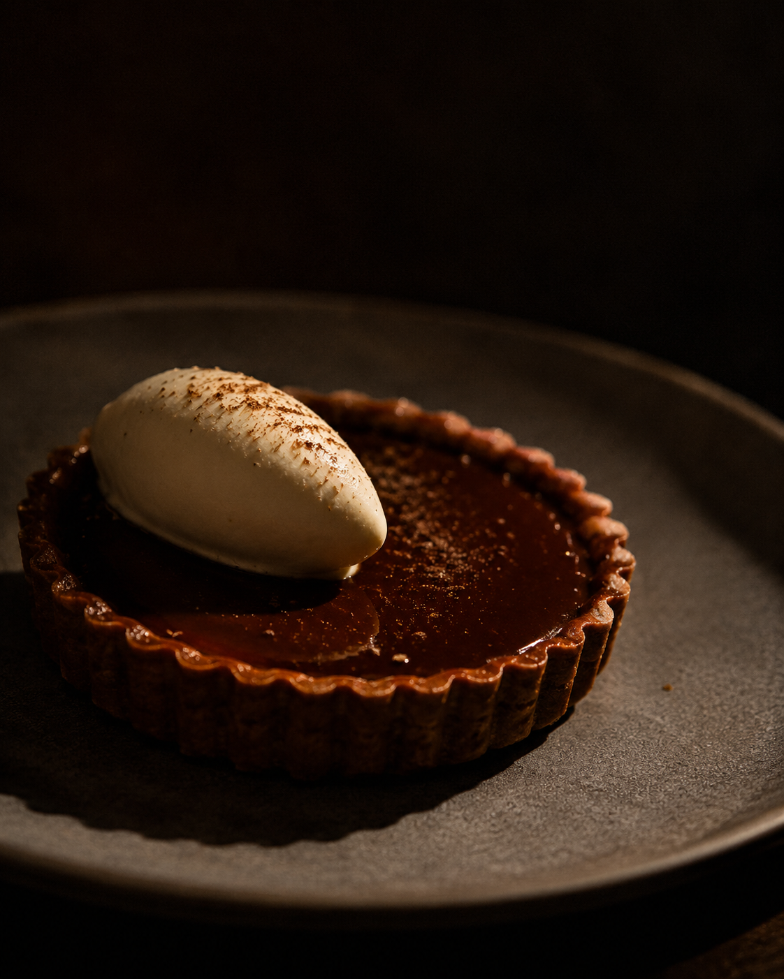 Dark miso caramel tart with a quenelle of crème fraîche, warm spotlight.