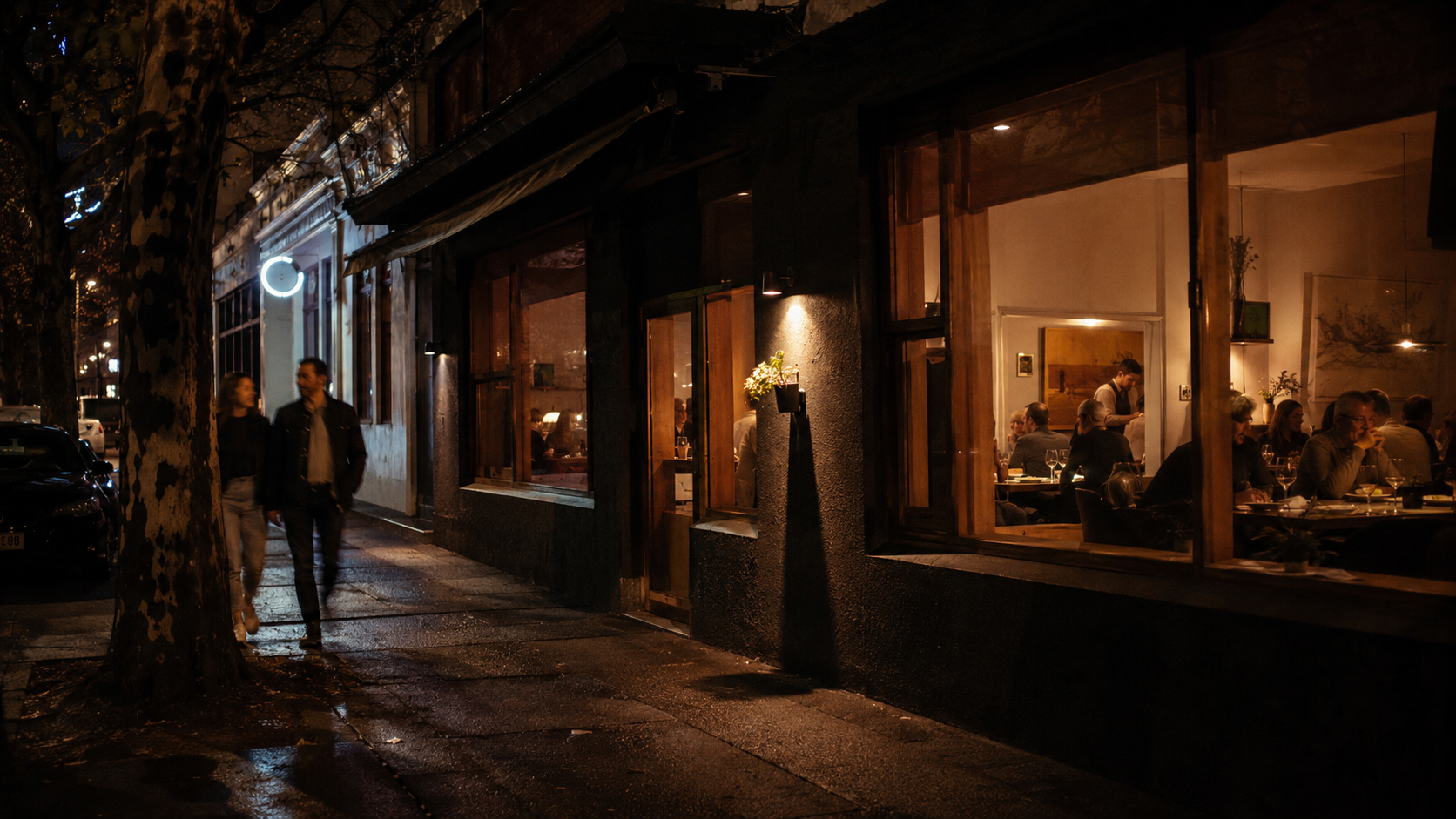 Ember House late at night on Gertrude Street — warm light spilling onto the dark Fitzroy footpath, the room glowing and inviting.