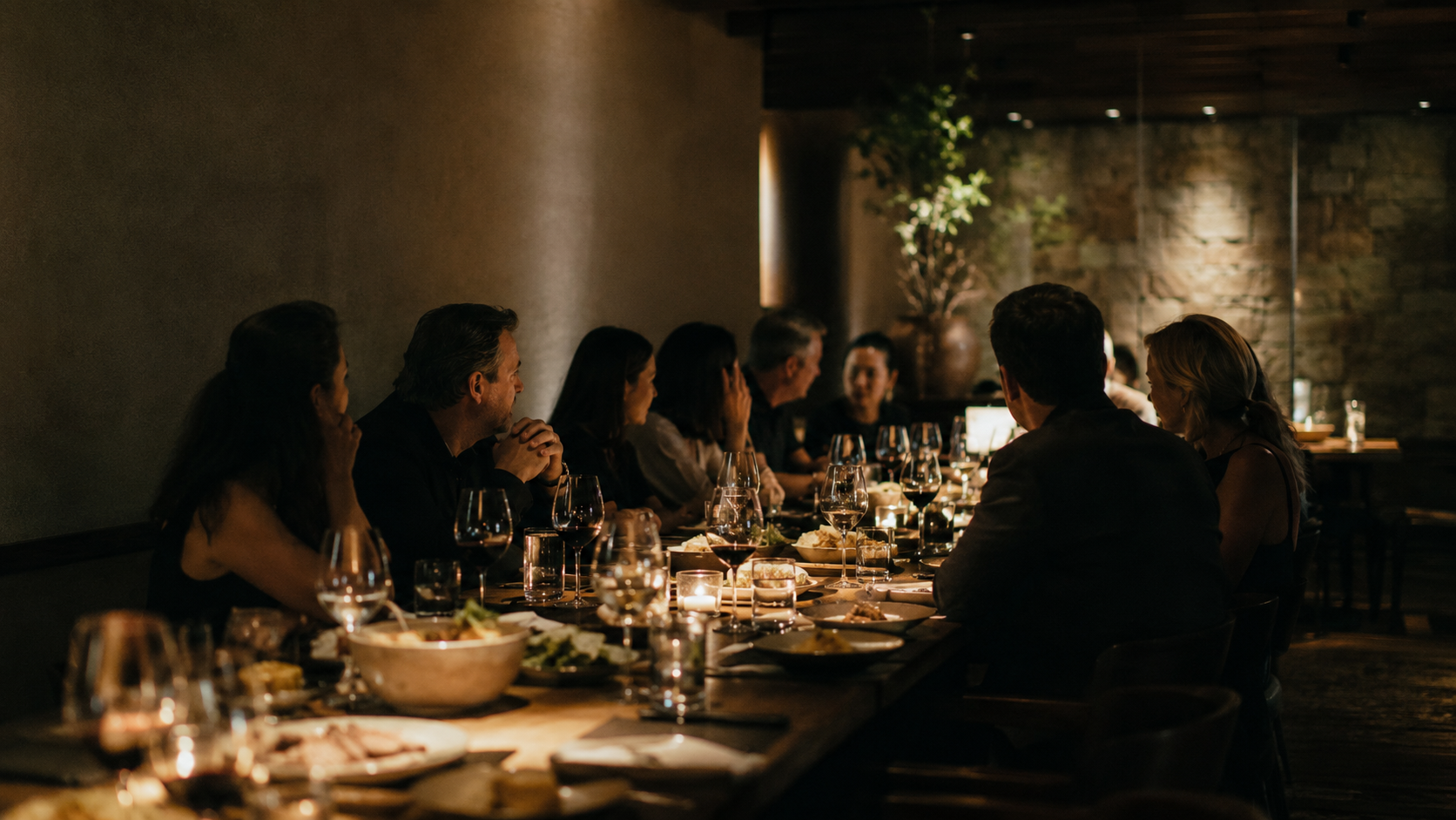 A long private dining table set at Ember House, candlelight and glassware down its length, a group celebration in a moody room.